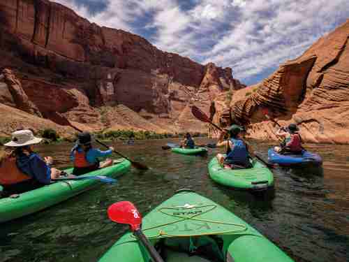Shot from the perspective of a person in a kayak, several kayaks with students float on a river in a canyon